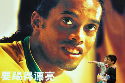 A man with a child in his arms walks past a billboard of Brazil soccer player Ronaldinho in Shanghai June 8, 2006. The Chinese words on the billboard, when translated, read: "To play a beautiful game". 
