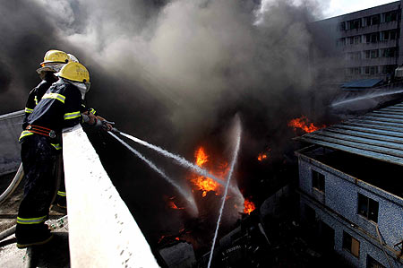 A girl plays a remote-control plane toy as smoke billows out from a shoe plant in Shenzhen south China's Guangdong Province, after a fire broke out there. The blaze lasted 12 hours before it was finally put out, engulfing a warehouse and a workshop. No casualty was reported. [gd.southcn.com]