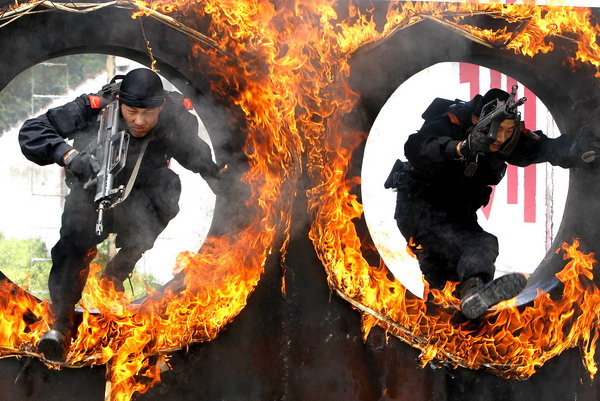 Two officers with the Armed Police Beijing brigade spring through fire loops during an anti-terrorist drill on June 30. Terrorists to be named, assets seized