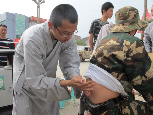 Shi Yanyun, a rescue team member from Shaolin Temple, treats a volunteer who hurt his back during earthquake rescue operations in Lushan, Sichuan province, on Thursday. AN BAIJIE / CHINA DAILY Shaolin monk doctors assist earthquake victims