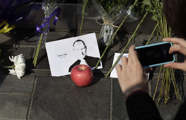 An iPhone4 user takes a picture of Steve Jobs, which was placed with an apple and flowers, next to the entrance of an Apple retail store in Beijing's Sanlitun October 6, 2011. The world mourns Steve Jobs
