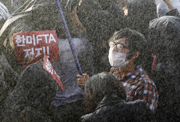 A protester tries to march towards the National Assembly as riot police use water cannons to disperse the rally against the South Korea-US free trade agreement (FTA) talks in Seoul Nov 3, 2011. The red banner reads: 'Block the South Korea-US FTA!' South Koreans protest free trade agreement with US