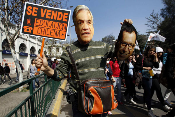 A demonstrator wears a mask of Chile's President Sebastian Pinera as he holds a banner that reads 'Chilean education is sold' and a Interior Minister Rodrigo Hinzpeter mask during a student rally against the government's public education system in Santiago city September 22, 2011. Chile: Students riot demanding education reform