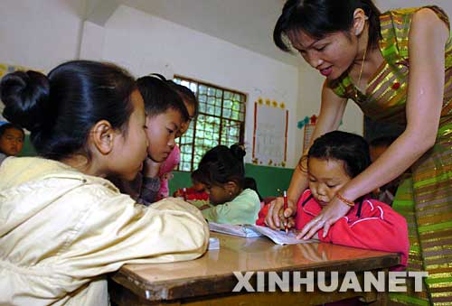 2004年12月3日，云南省西雙版納傣族自治州景洪市勐罕鎮(zhèn)曼聽村的黨員、教師玉罕約（右一）在給村小學(xué)的孩子們補(bǔ)習(xí)功課。曼聽村是一個(gè)典型的傣族村寨，近兩年來，曼聽村黨支部大力加強(qiáng)基層黨組織建設(shè)，村黨支部充分發(fā)揮黨員在經(jīng)濟(jì)建設(shè)中的作用，帶領(lǐng)群眾學(xué)科技、調(diào)結(jié)構(gòu)、闖市場，開辦科技講座和黨課培訓(xùn)，使得村里經(jīng)濟(jì)發(fā)展迅速，人民生活明顯改善。 新華社發(fā) 