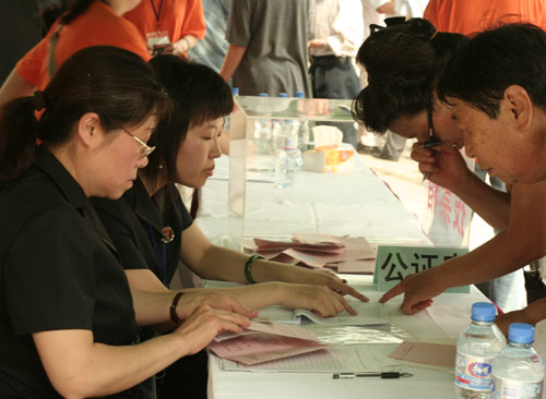 Two notary officials check the documents of voters at the venue for a vote on demolishment and reconstruction of old buildings in Juixiaqiao Sub-district in Beijing, June 9, 2007. Local government and the real estate developer jointly organize the vote on Saturday to see if majority residents of over 5000 families accept the new compensation policy after failed attempts to reach an agreement through other ways. Both notary officials and supervisors are invited to monitor the vote that runs from 9 a.m. to 9 p.m. at six ballot booths. [Sun Yuqing/www.midnightarchive.com]